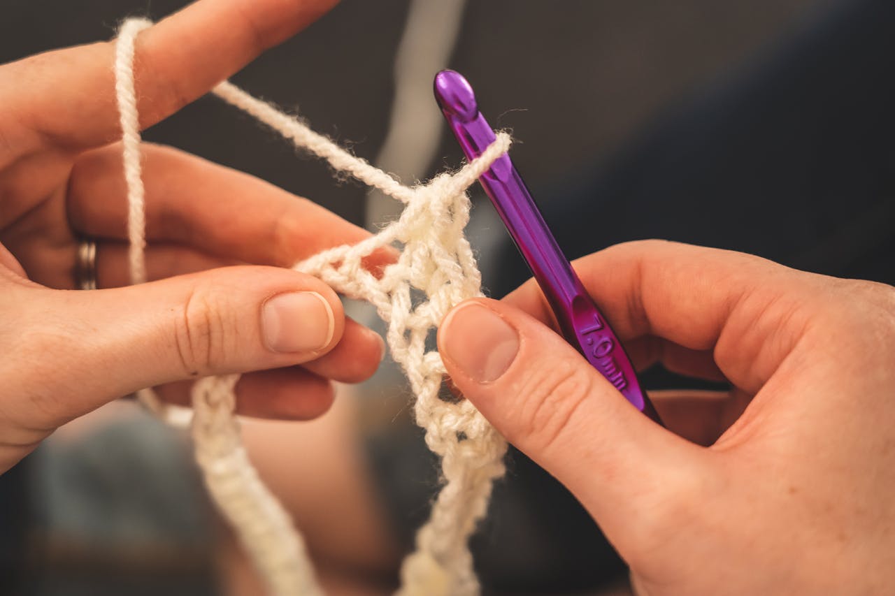 Hands crocheting with a purple hook, showcasing intricate yarn details.