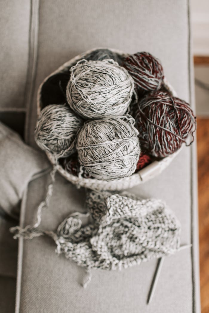 Basket filled with yarn balls, needles, and knitted fabric on a cozy armchair.